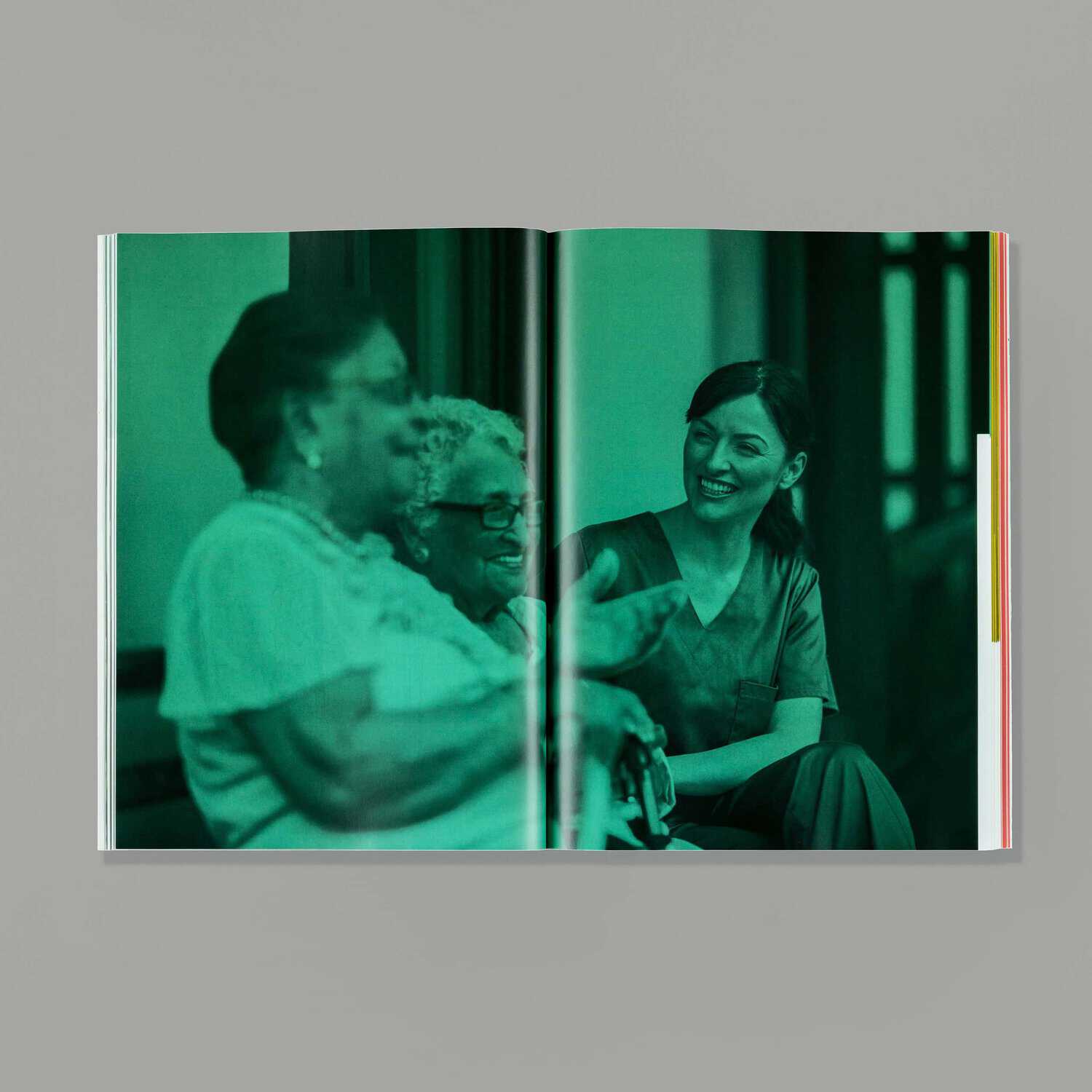 An open book reveals a photo of three people sitting together—two elderly individuals and a younger person in uniform, immersed in conversation. The greenish tint evokes the timeless essence of learning to care across generations.