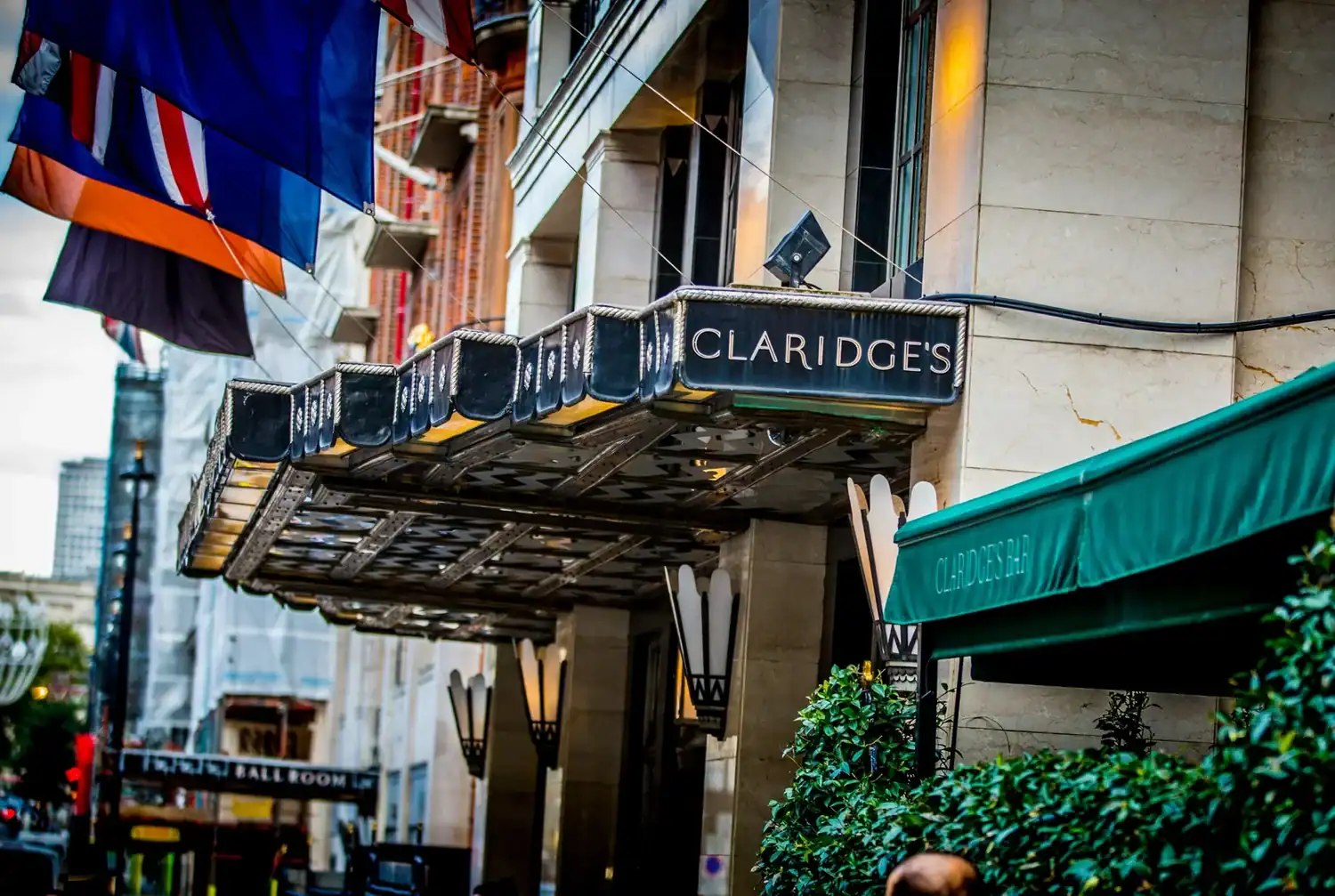 The entrance of Claridge's hotel, adorned with a decorative awning and flags, beckons like a stage set for culinary heroes, viewed elegantly from the street.