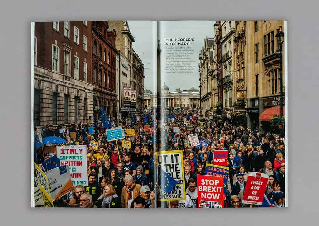 The magazine spread captures a large crowd at a street protest in support of Brexit, with signs held high. The streets, lined with buildings, echo the bustling energy reminiscent of a London Press Club event. In the background, a statue stands watch over this historic moment.