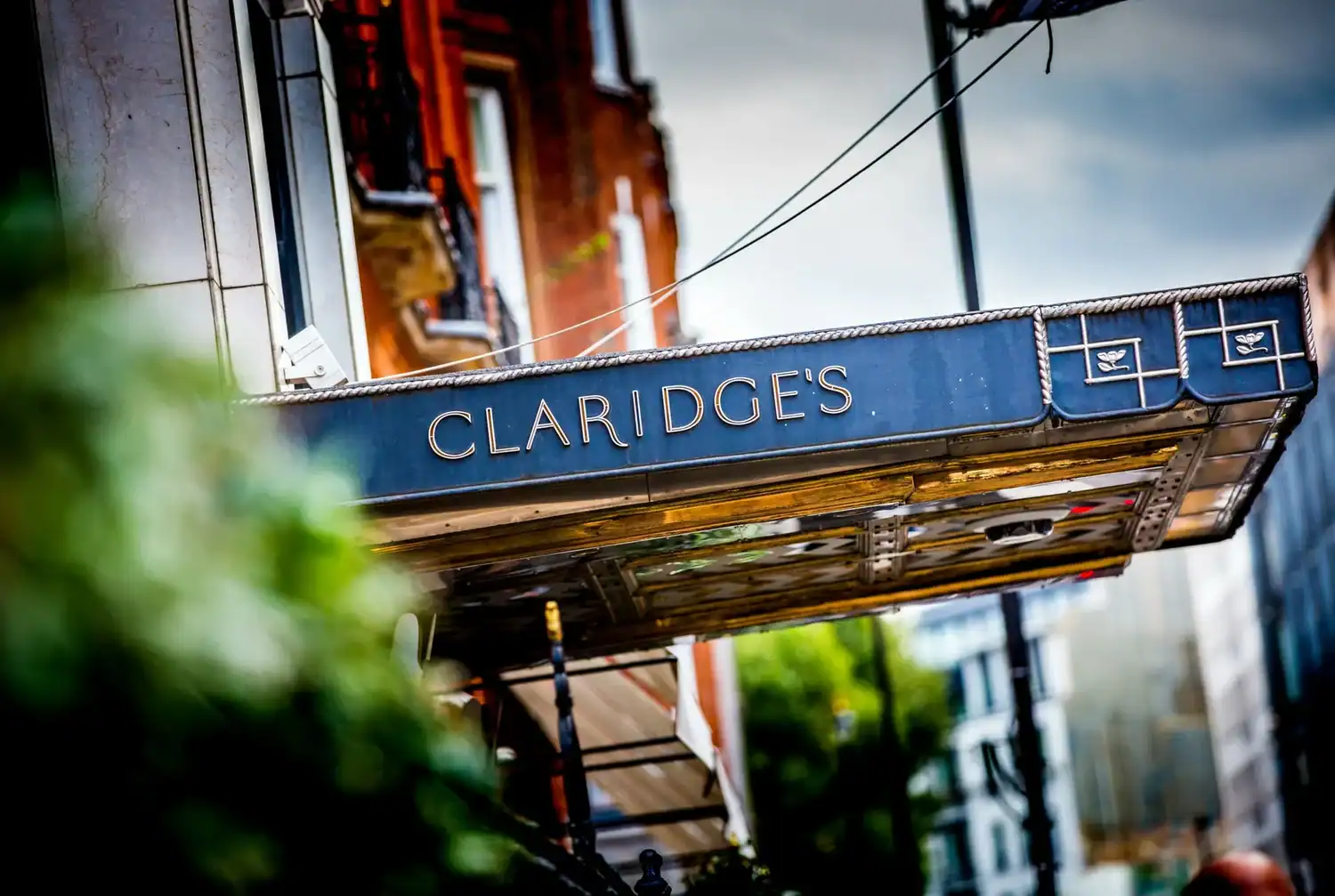 Street view of a building with "Claridge's" on a metal canopy, where urban elements blend with greenery. Like unsung heroes, dedicated chefs inside transform fresh ingredients into culinary masterpieces.