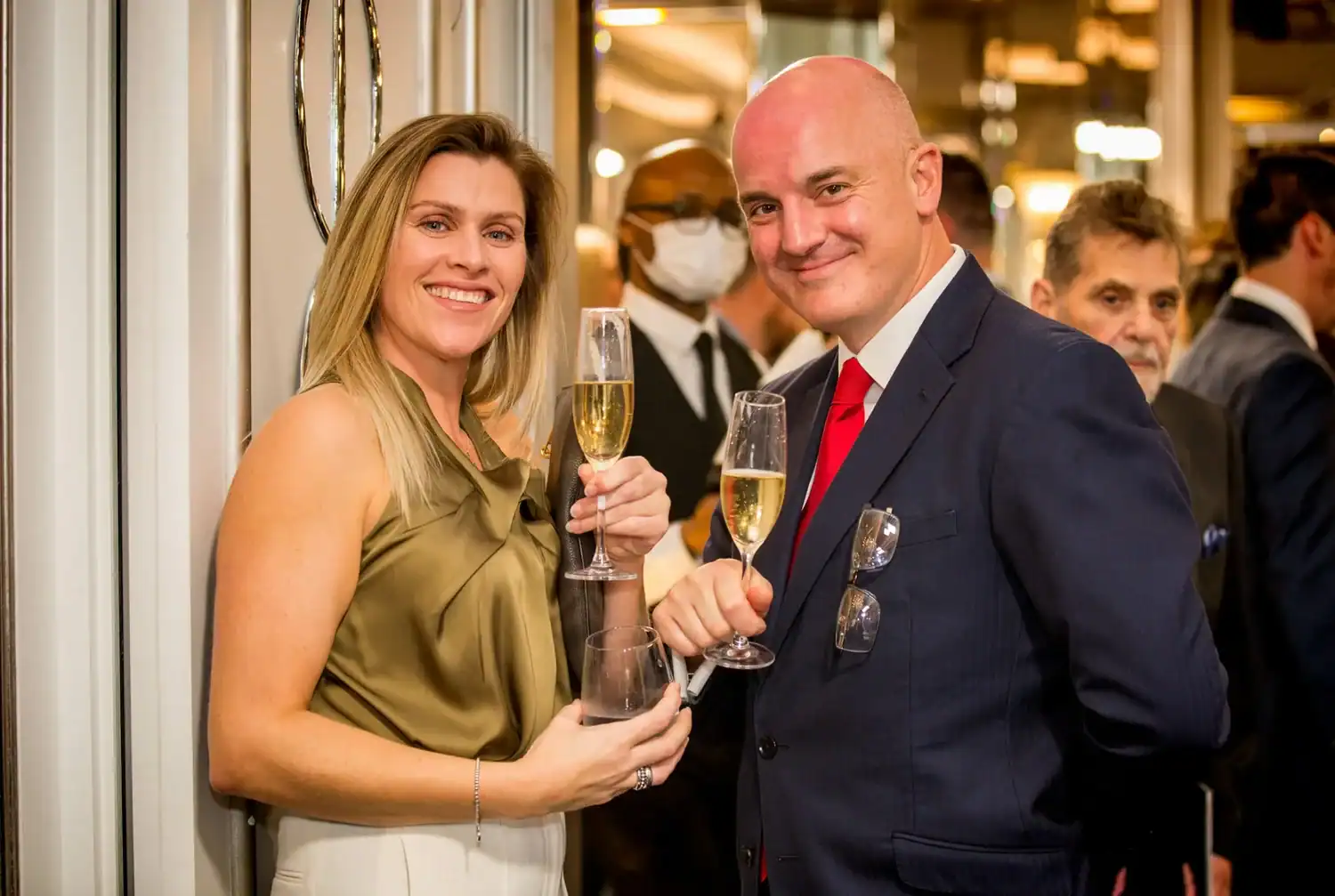A woman and a man in formal attire hold champagne glasses at a social event, toasting like heroes celebrating their culinary triumphs.