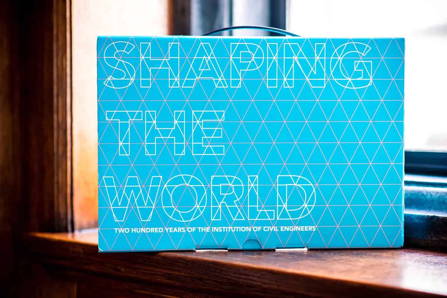 A blue geometric-patterned box with "Shaping the World" elegantly inscribed, celebrates two hundred years of the Institution of Civil Engineers, thoughtfully placed on a window sill.