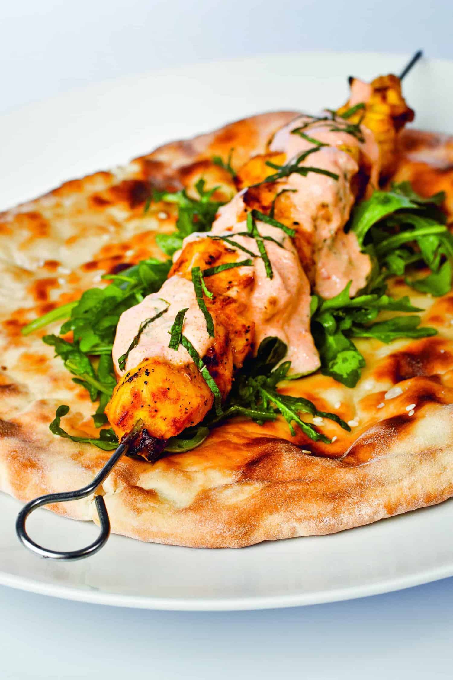 Savor the taste of history with our grilled skewer on flatbread, a dish worthy of being featured in any RAF 100 cookbook. It's topped with creamy sauce and fresh greens for an unforgettable culinary experience.
