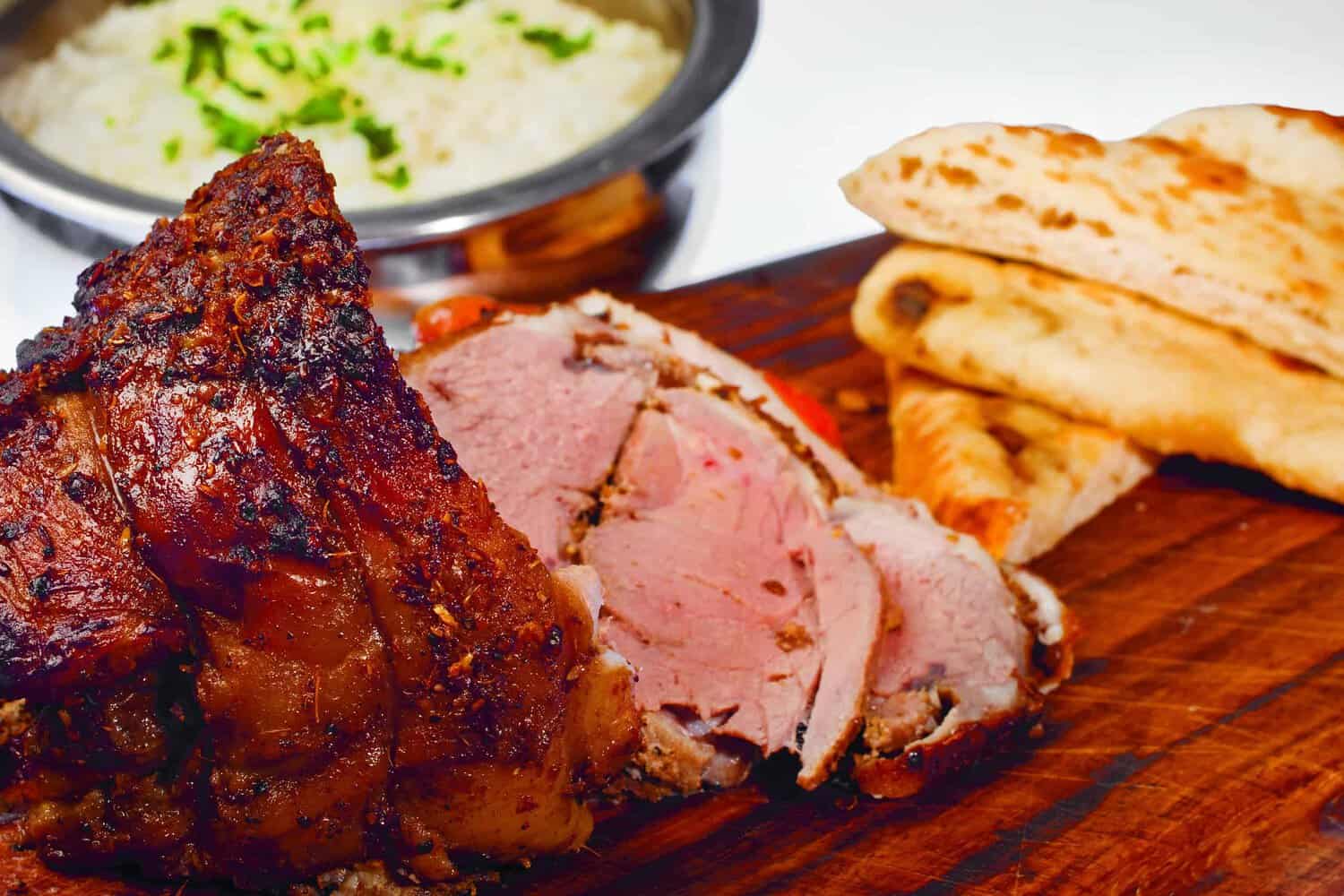 Roast meat slices rest on a wooden board, accompanied by naan bread and a fragrant dish of rice garnished with herbs—an enticing spread reminiscent of recipes found in a classic cookbook.