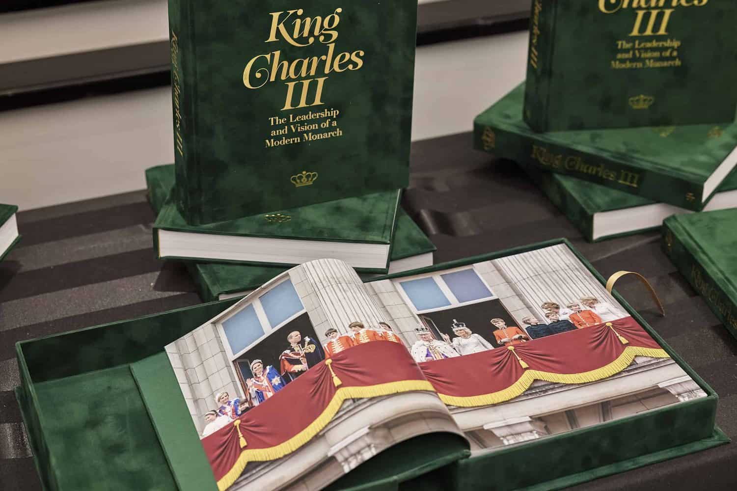 A stack of green books titled "King Charles III: The Leadership and Vision of a Modern Monarch" features an open book with a royal family photo on a balcony, capturing the essence of the British monarchy.