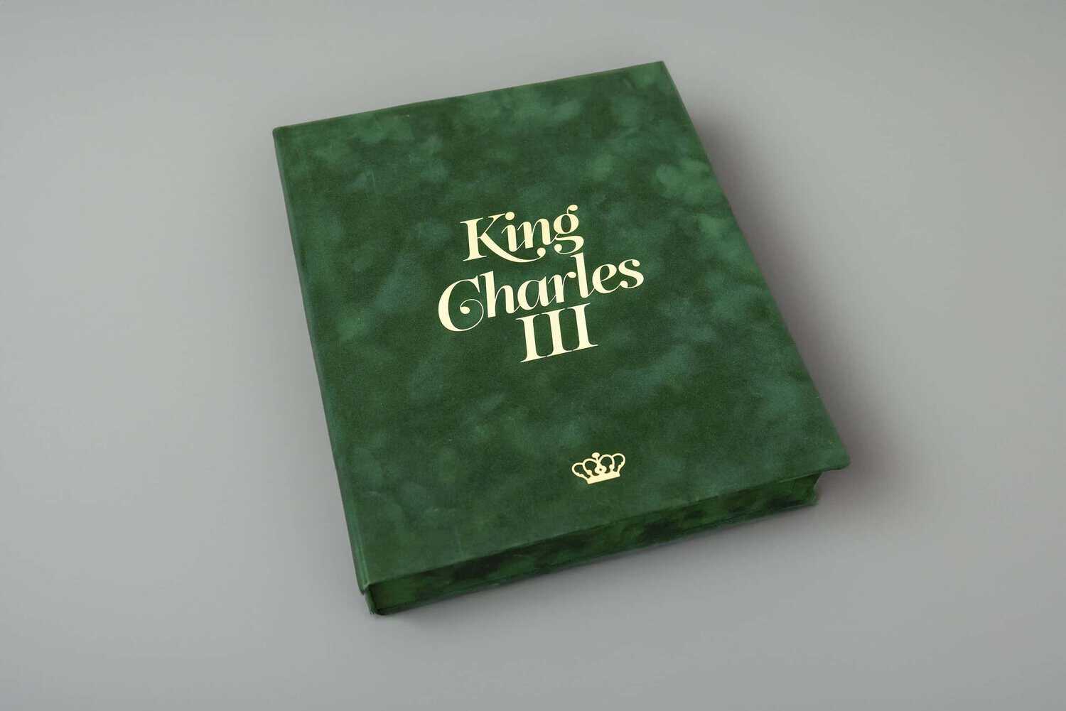 A regal green book, adorned with the gold text "King Charles III" and a crown symbol, rests elegantly on a plain surface.