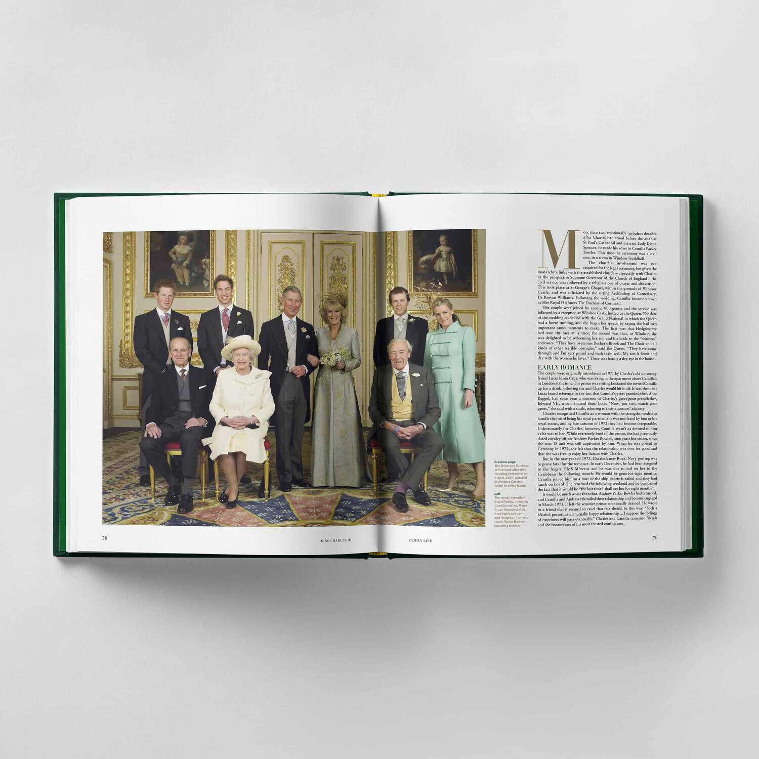 An open book reveals a formal portrait of King Charles III and eight others in elegant attire, posed in a lavish room, with a block of text on the right page.