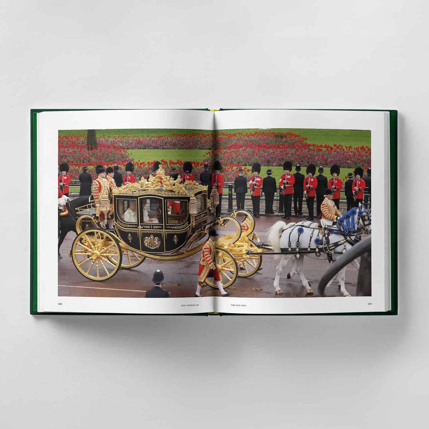 An open book reveals a royal carriage procession featuring King Charles III, with white horses and guards in red uniforms, set against a floral background.