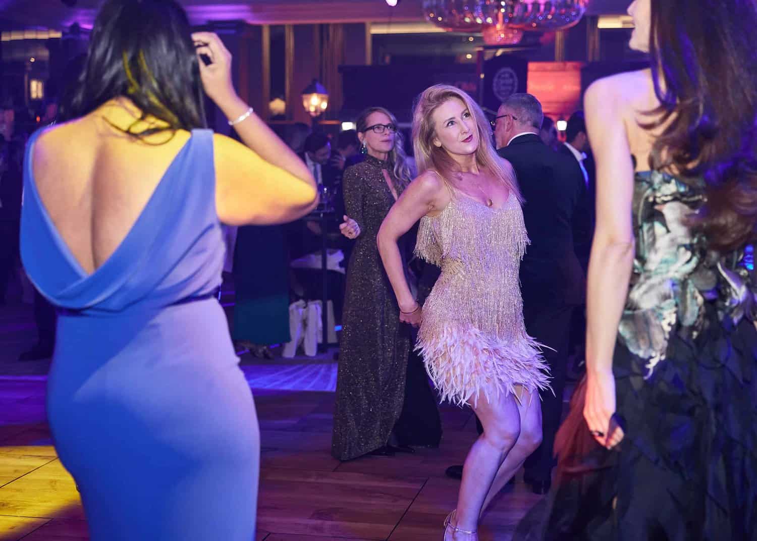 People dancing at the Press Club Ball, with a woman in a light dress striking a pose. The ballroom, alive with colorful lights, captures the elegance of the London Press Club event.