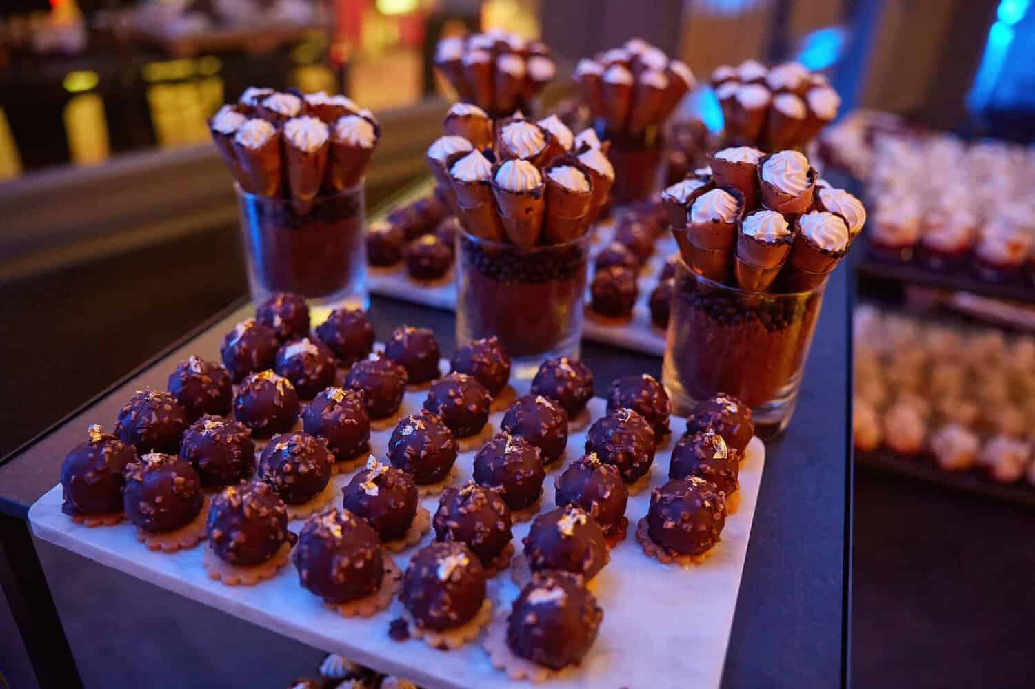 Assortment of chocolate truffles and cream-topped cones displayed on trays and in glass containers, adding a touch of indulgence to the dimly lit London Press Club event.