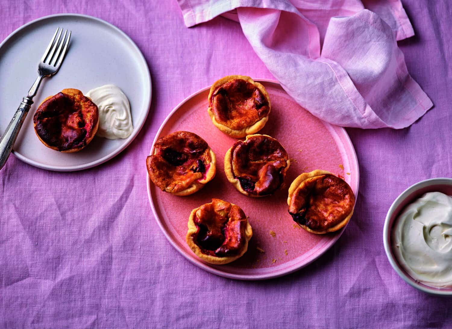 Six small pastries on pink plates with a side of cream, set on a pink tablecloth with a fork, are the true heroes of any cooking adventure.