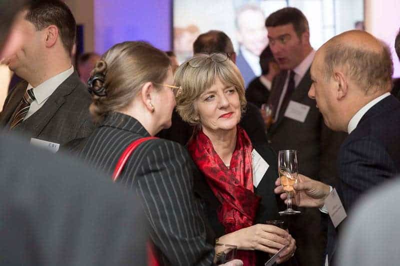 At a networking event celebrating 50 years of business innovation, people in formal attire engage in conversation while holding drinks.