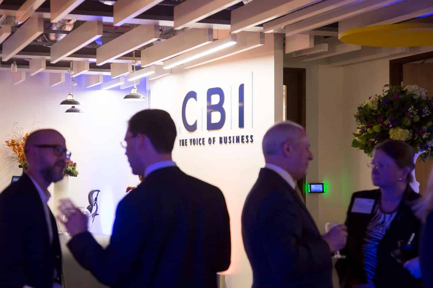 People networking at a business event with the CBI sign in the background, celebrating 50 years of business innovation.