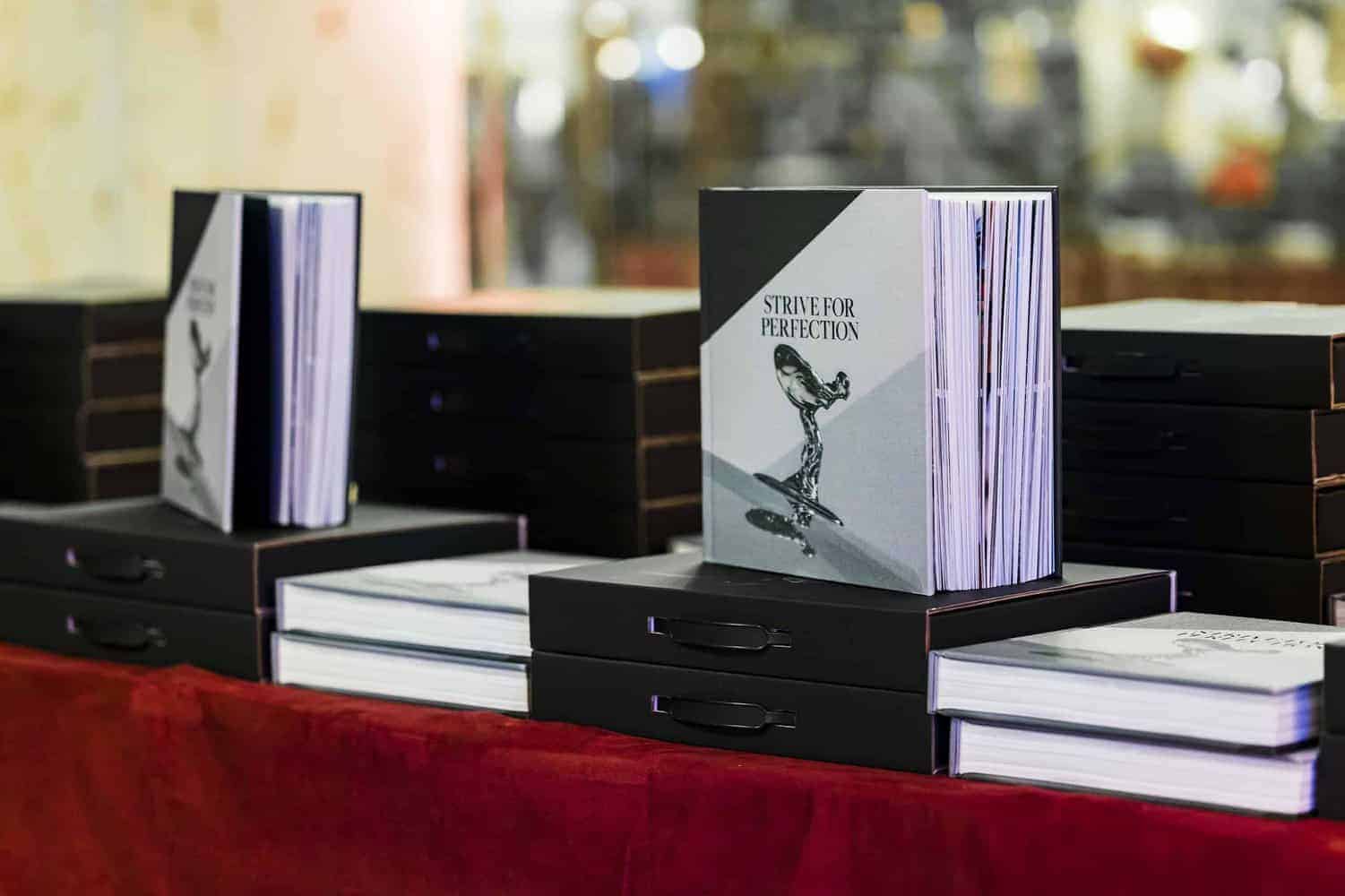 Stacked books titled "Strive for Perfection" with a hardcover design and a black-and-white cover image of a statue, epitomizing the essence of perfectionism, displayed on a striking red surface.