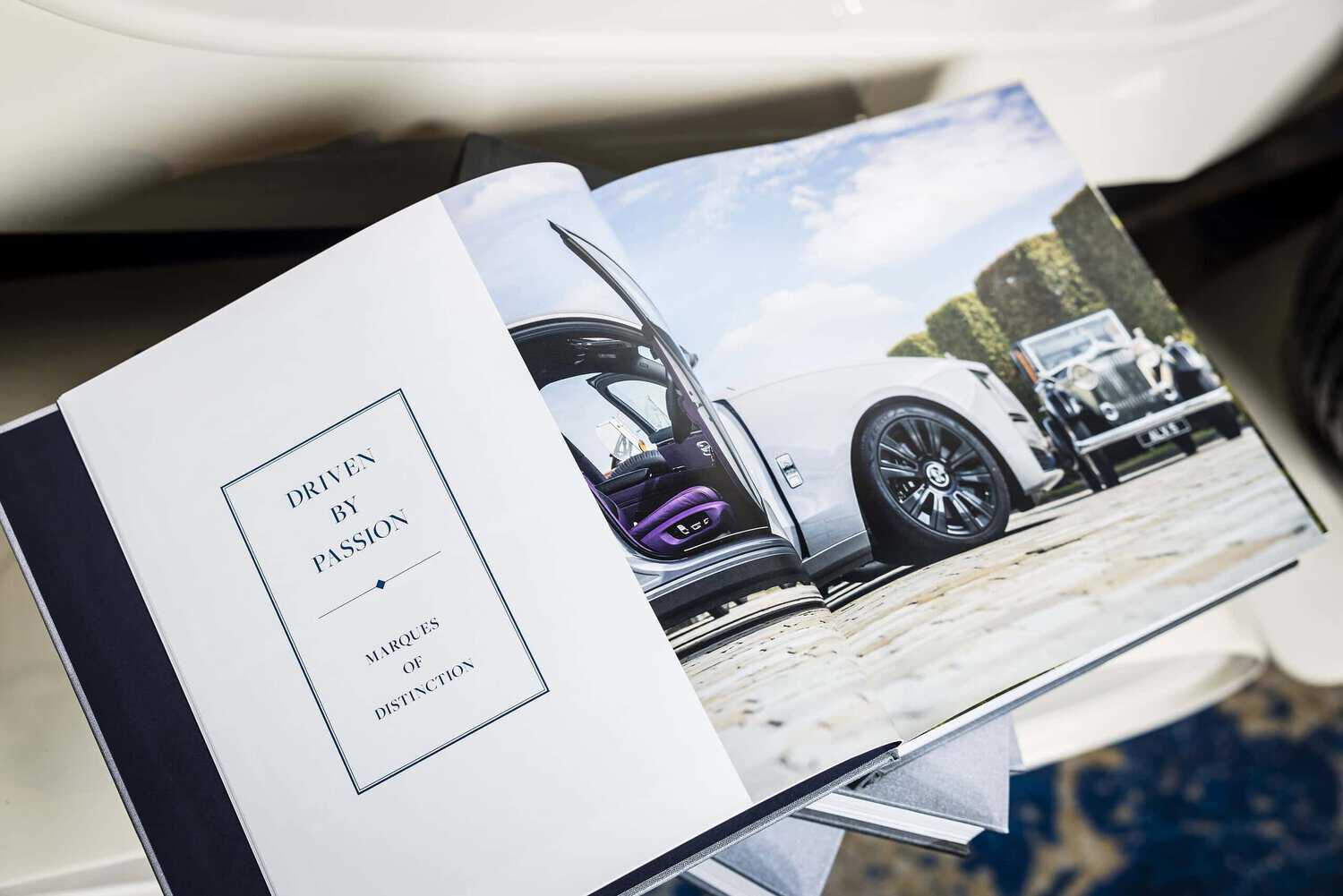 An open book showcases a luxury car with its doors ajar on one page, while the text "Driven by Passion: Marques of Distinction" graces the other. This image captures the essence of those who strive for perfection in every detail.