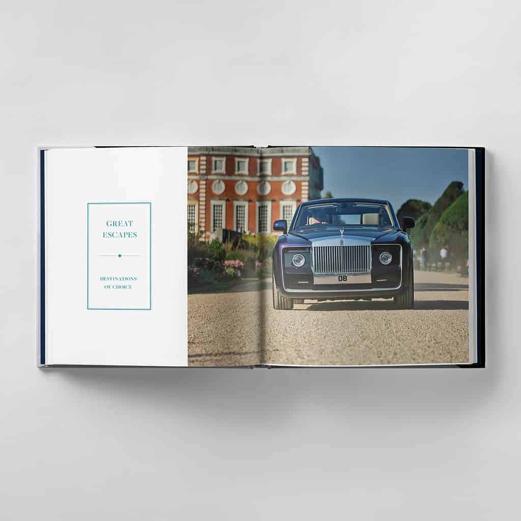 An open book rests on the table, its pages revealing a stunning photo of a Rolls-Royce gracefully navigating through a garden, with a historic building in the background—a true embodiment of striving for perfection.