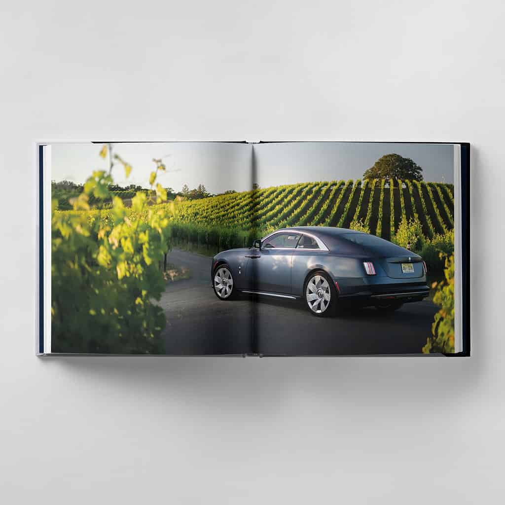 An open book reveals a luxury car driving through a scenic vineyard, embodying the perfection of harmonious design.