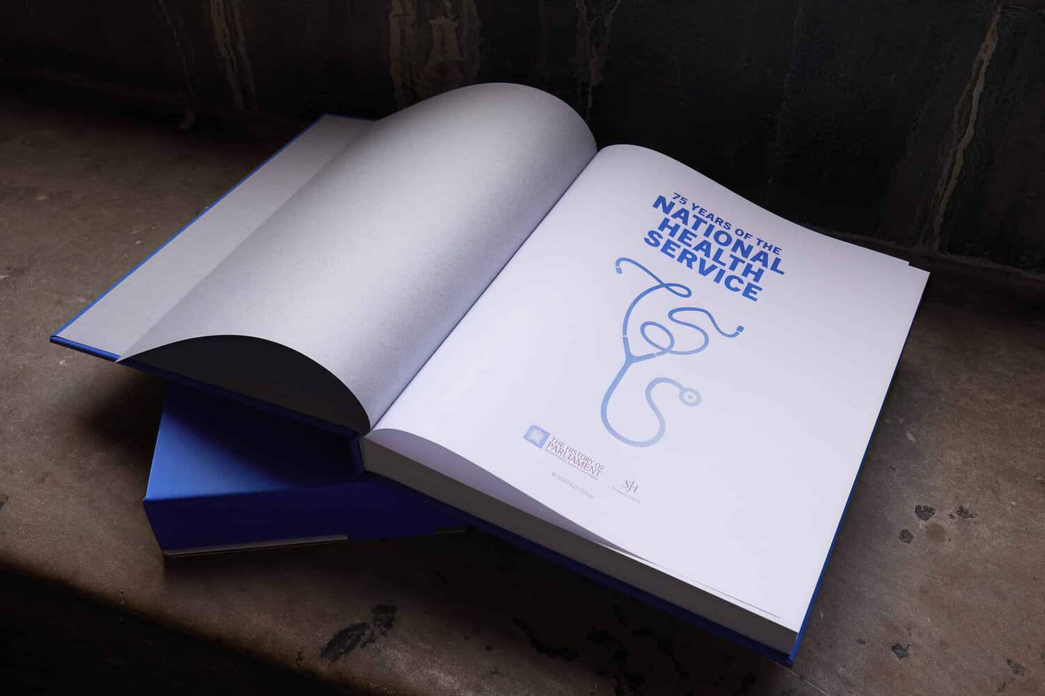 Open book on a gray surface, titled "75 Years of the NHS," featuring a symbol resembling a caduceus on the title page.