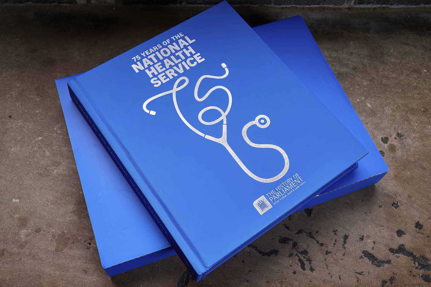 Two blue books titled "75 Years of the National Health Service" feature a stethoscope design on the cover, celebrating the NHS anniversary.