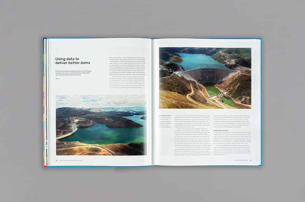 The open book on a gray surface reveals pages on dams, enriched with aerial photos and text exploring data usage for dam improvement—a testament to sustainable engineering efforts in line with the UN75 initiative.