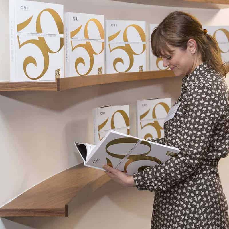 A person engrossed in a magazine on business innovation stands before a display showcasing several copies of the same edition on wooden shelves.