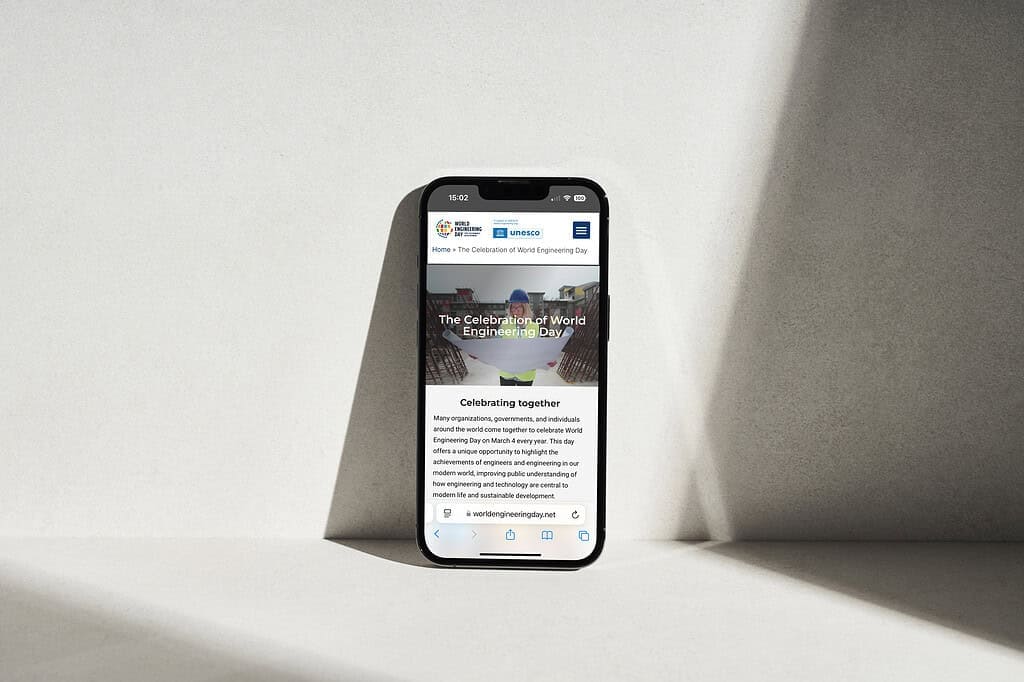 A smartphone elegantly displays the World Engineering Day website on its screen, celebrating innovation against a minimalist light background with subtle shadows.